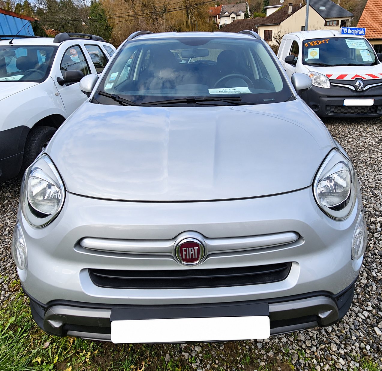 Fiat 500X grise vue de face, garée sur le gravier devant le garage.