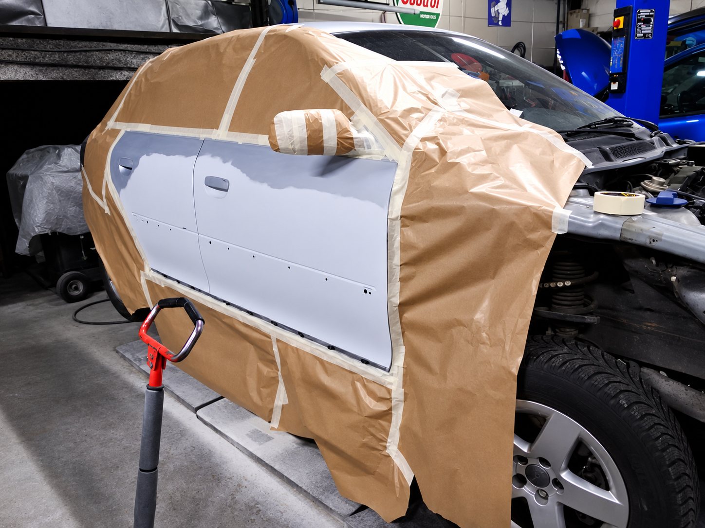Une voiture dans un atelier de carrosserie dont les portières, recouvertes d’apprêt gris clair, sont entourées de papier et de ruban de masquage avant la peinture.