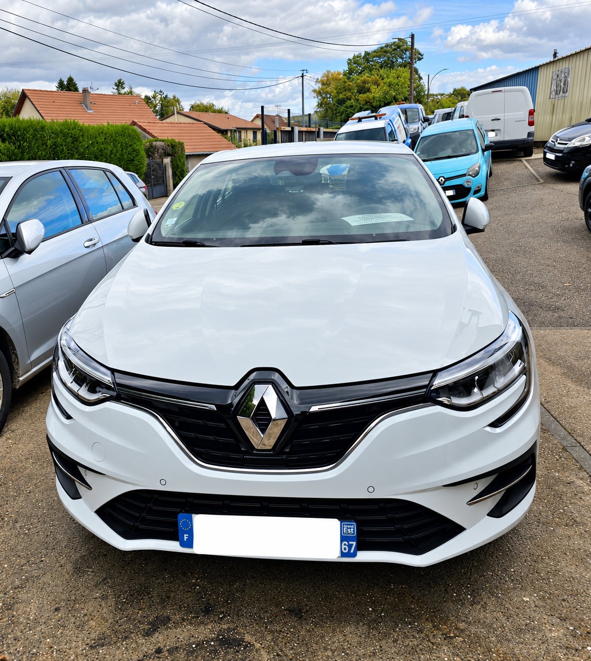Renault Mégane blanche vue de face sur un parking extérieur.